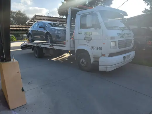 Grúa plataforma con auto frente a taller mecánico